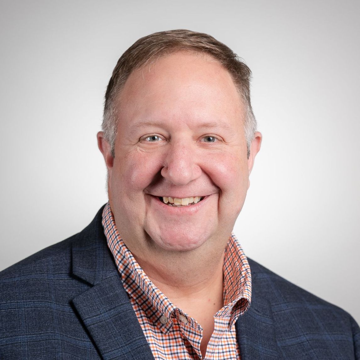 A man in a suit and plaid shirt is smiling for the camera.
