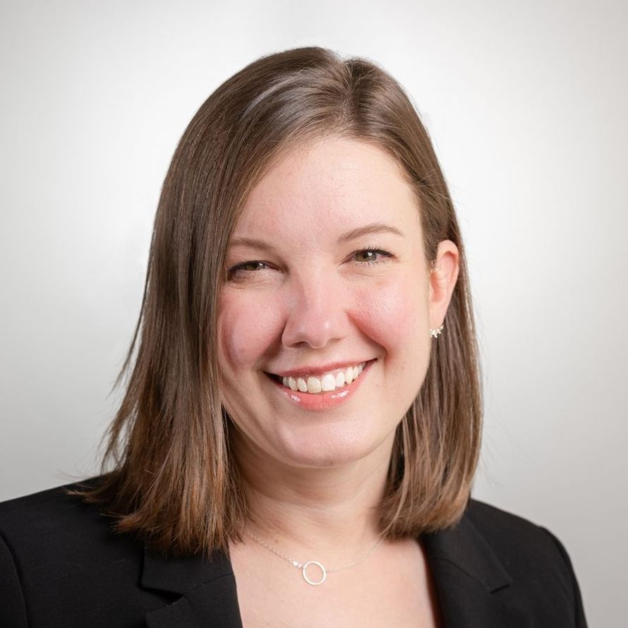A woman in a black jacket and necklace is smiling for the camera.