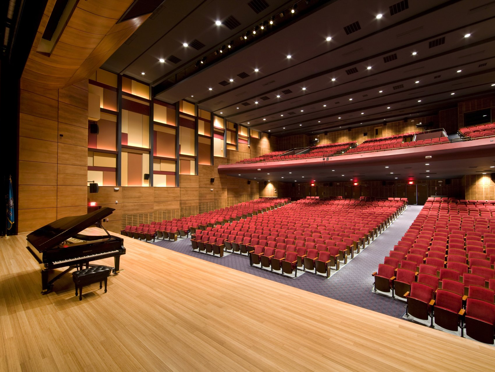 An empty auditorium with rows of red seats and a piano on stage