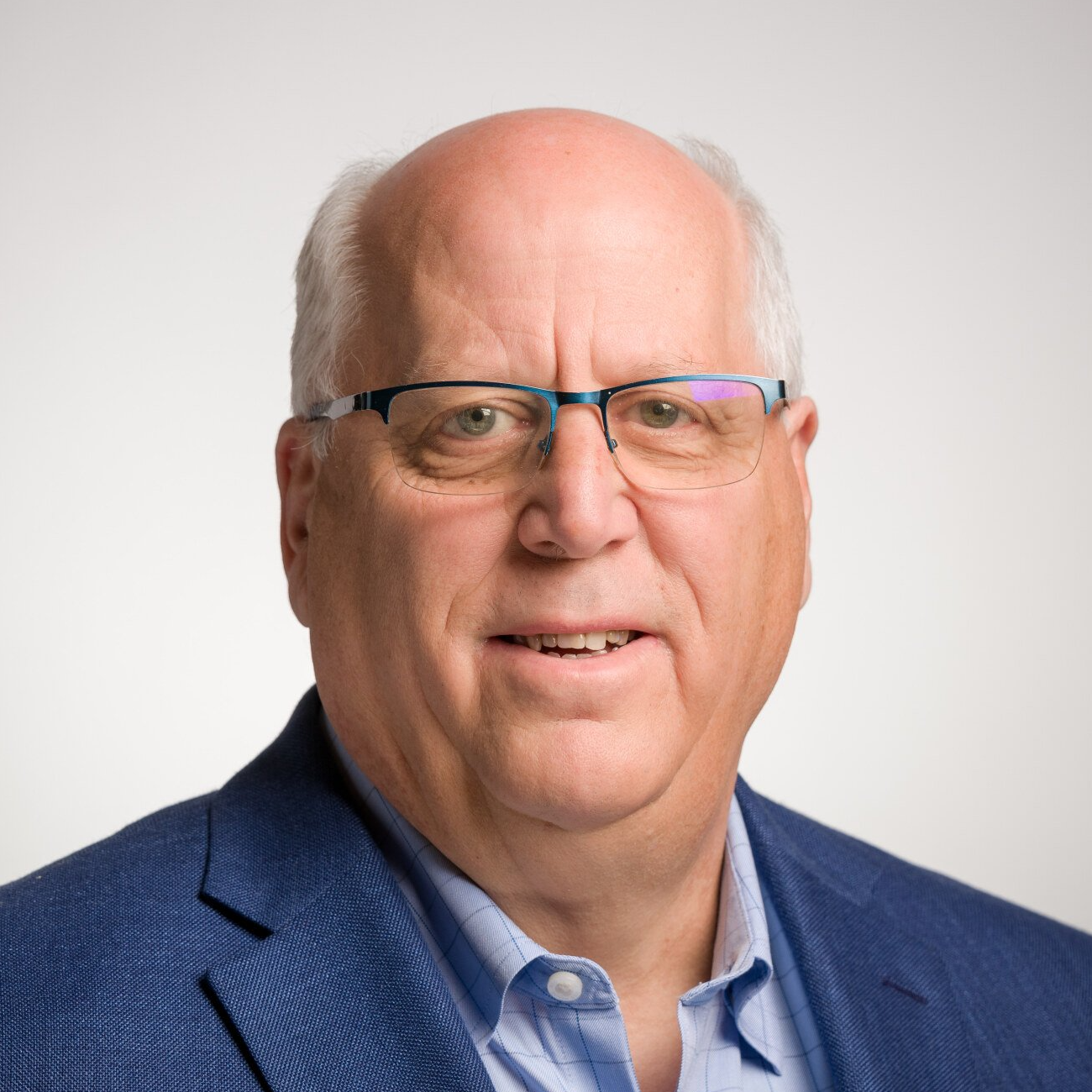 A bald man wearing glasses and a blue suit is smiling for the camera.