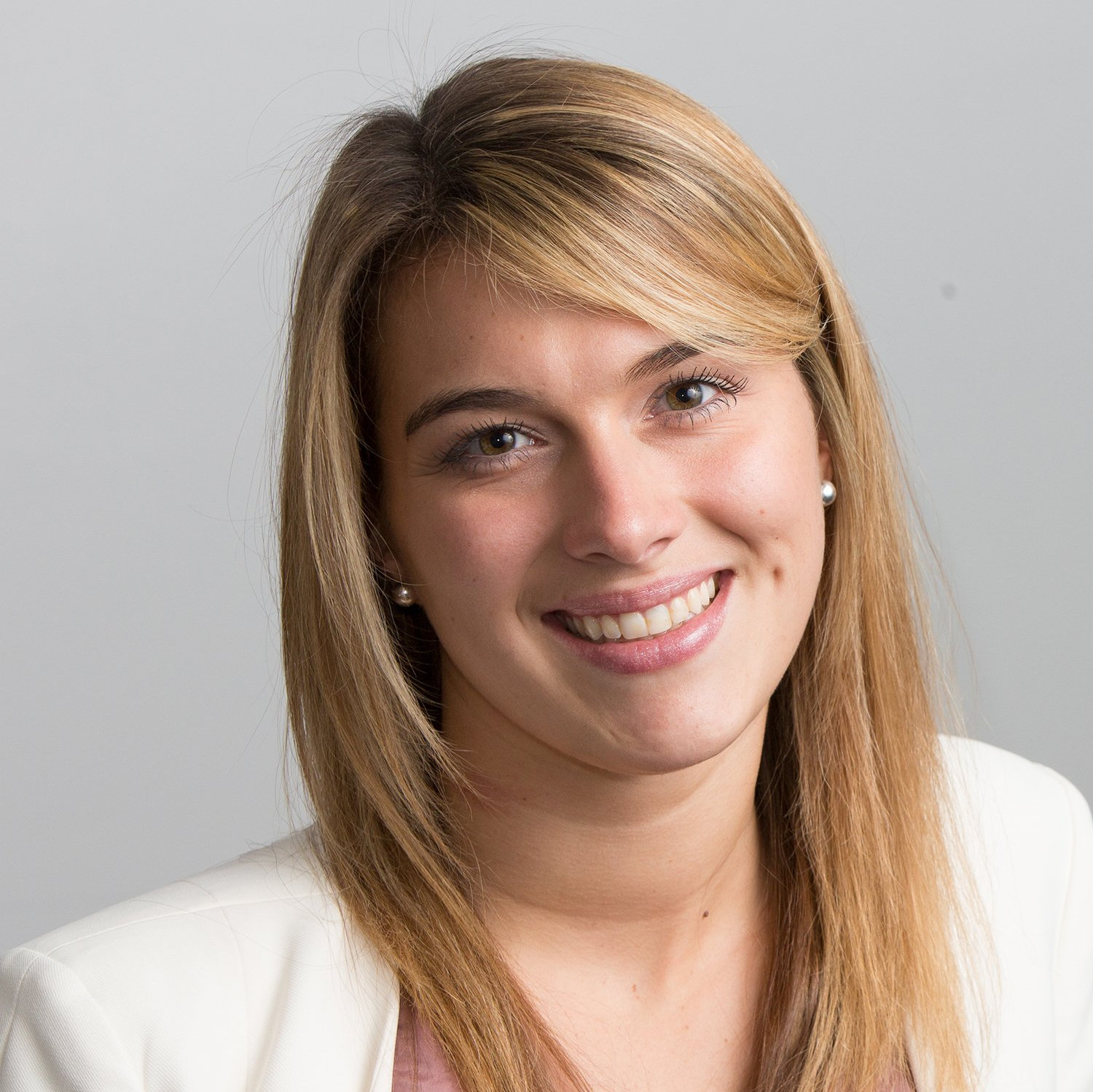 A woman with long blonde hair is smiling and wearing a white jacket.