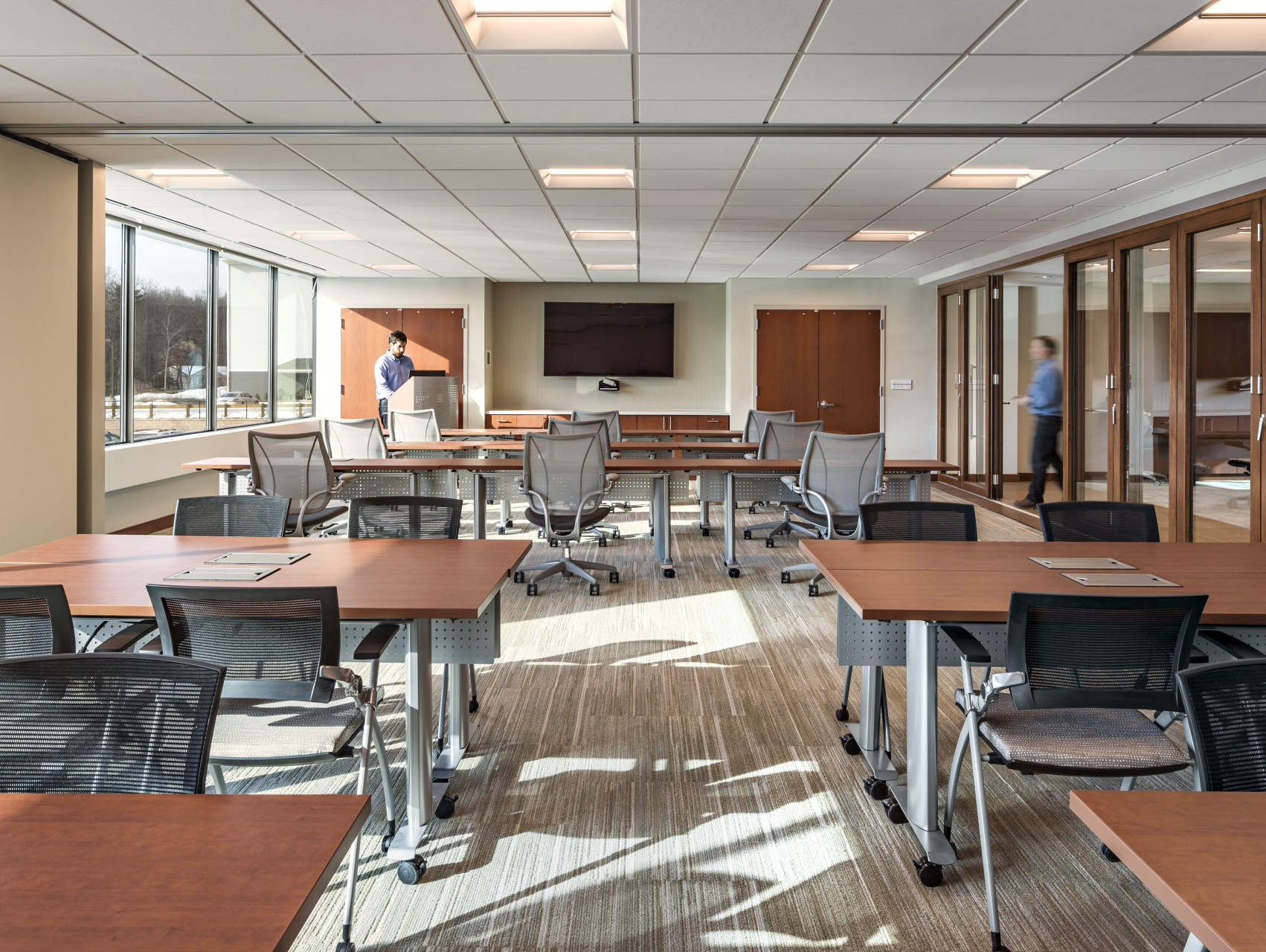A large conference room with tables and chairs and a flat screen tv.