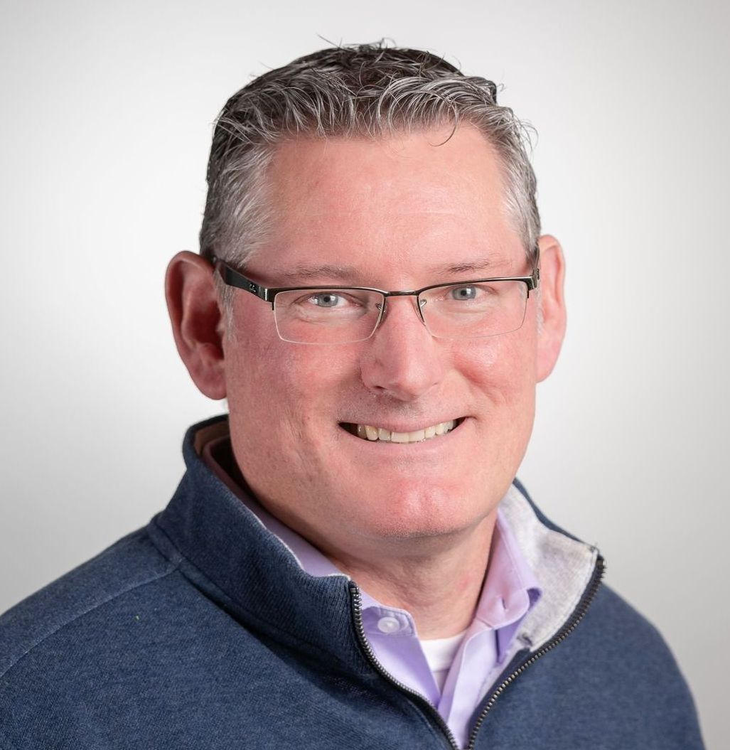 A man wearing glasses and a blue jacket is smiling for the camera.