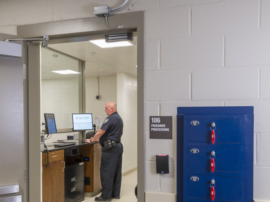A police officer is standing in front of a computer in a room.