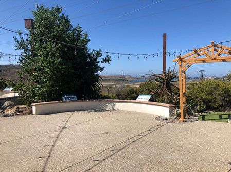 A patio with a curved wall, string lights, and a view of a marsh under a blue sky.