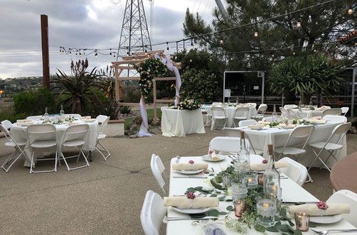 Outdoor wedding reception setup with white tables, chairs, decorations, and a floral arch.