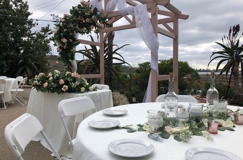 Wedding reception setup with floral arrangements on tables under a wooden arch.