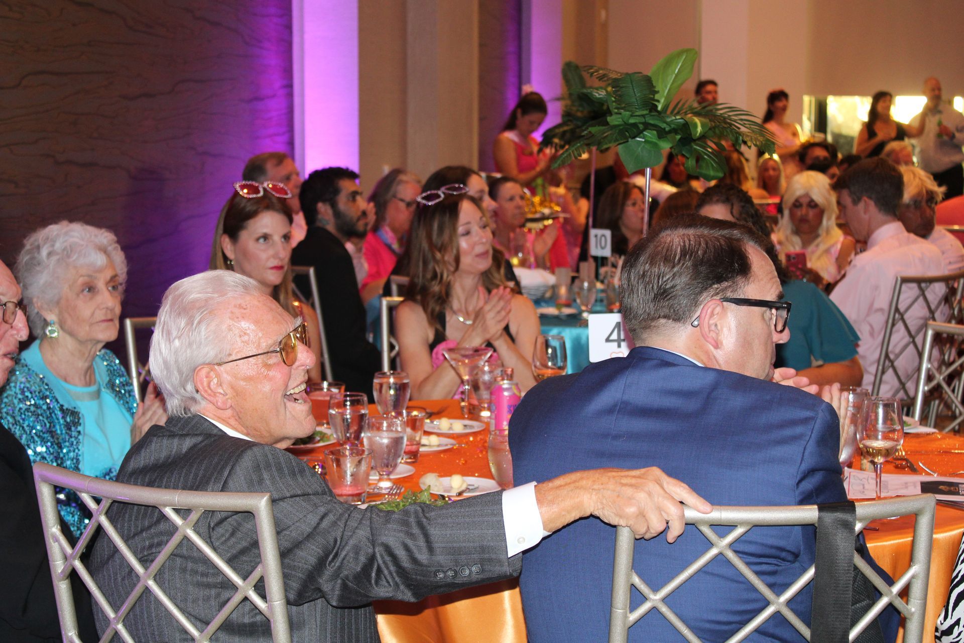 Guests seated at round tables in a warmly lit banquet hall, watching an event