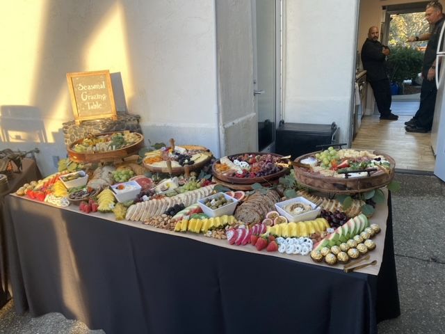 A large charcuterie spread on a table outdoors with a sign that says