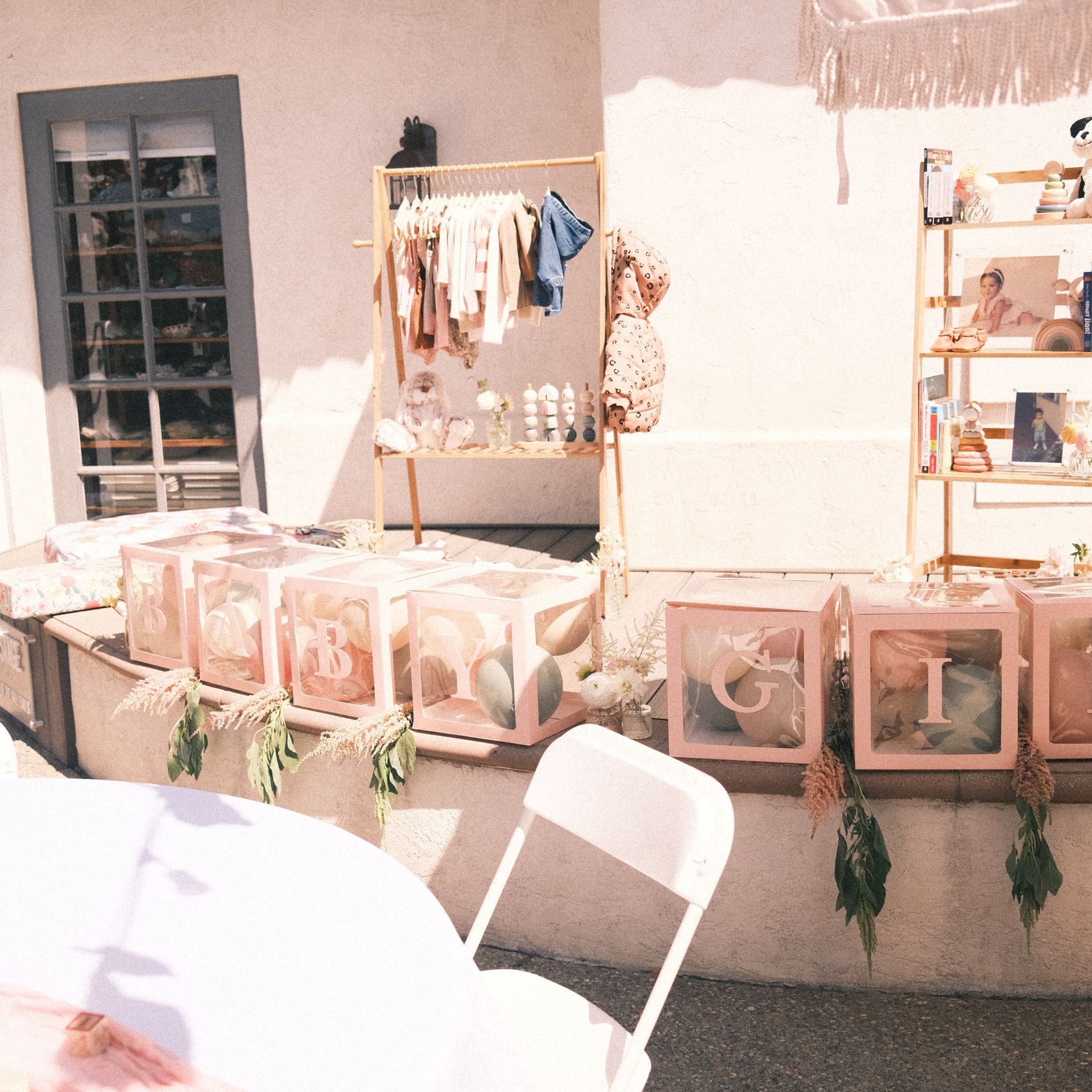 Baby shower decorations: pink boxes with letters, clothing rack, and shelving with decor.