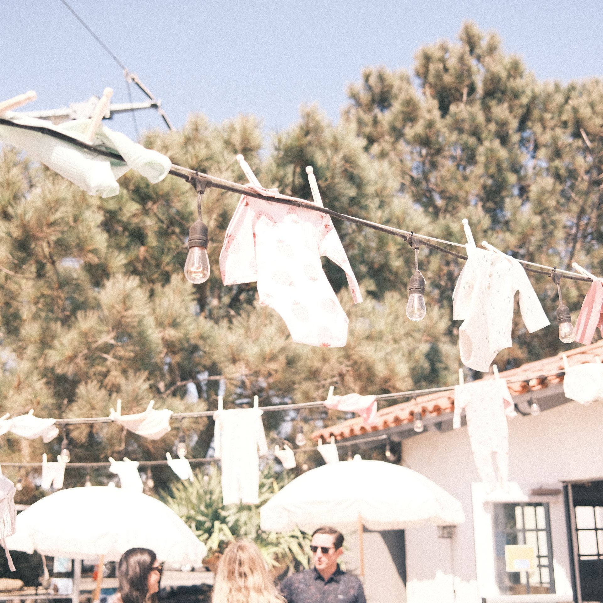 Laundry hung on a line strung between light fixtures outdoors. People and umbrellas are visible below.