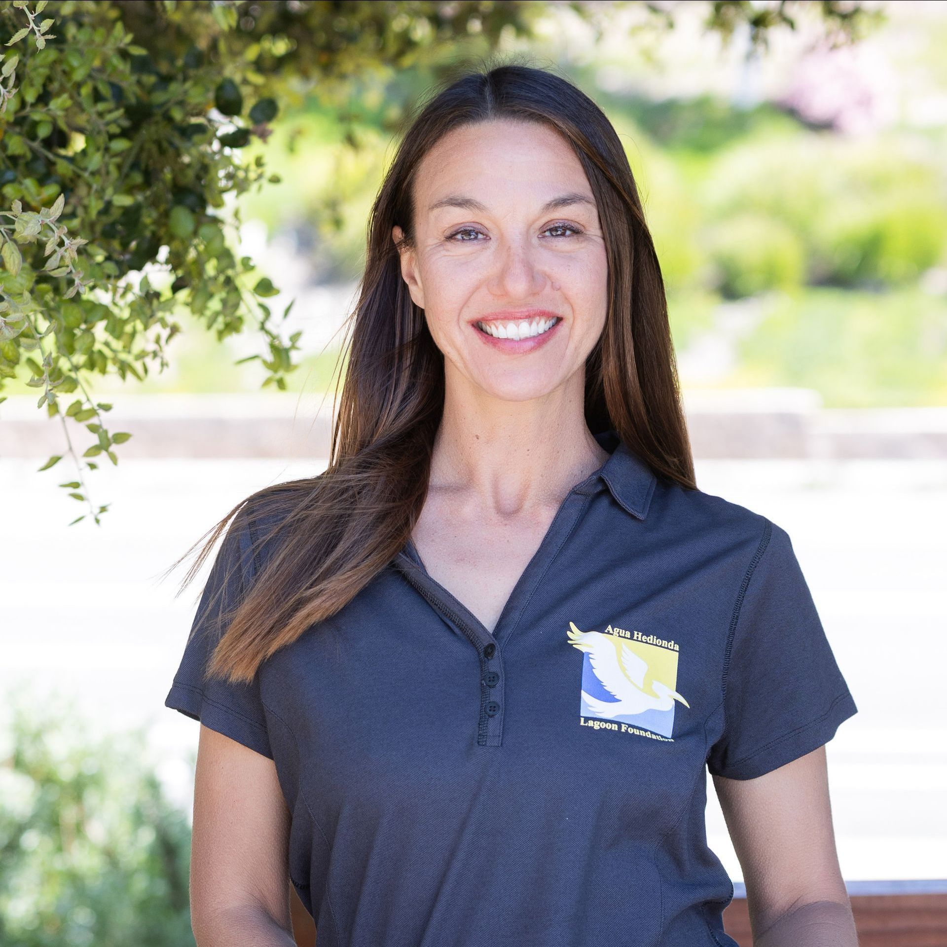 Woman with brown hair and a light blue shirt smiles outdoors.