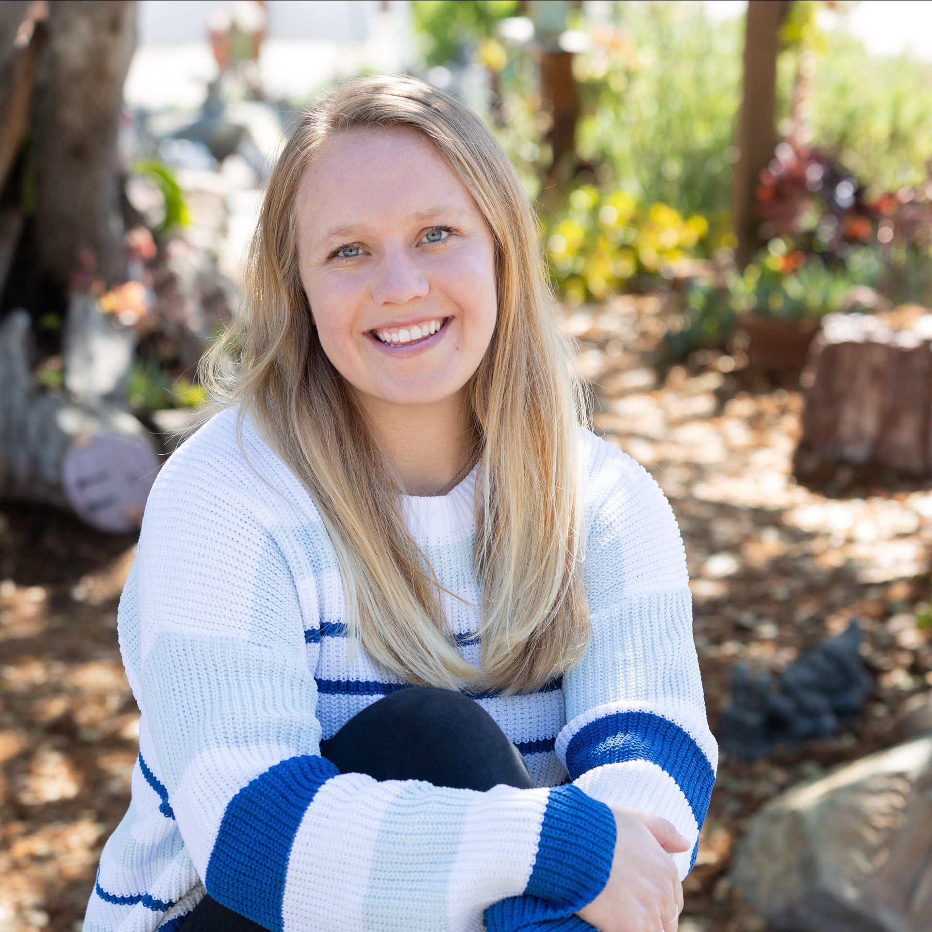 Woman smiles, wearing blue and white striped sweater, sitting outside.
