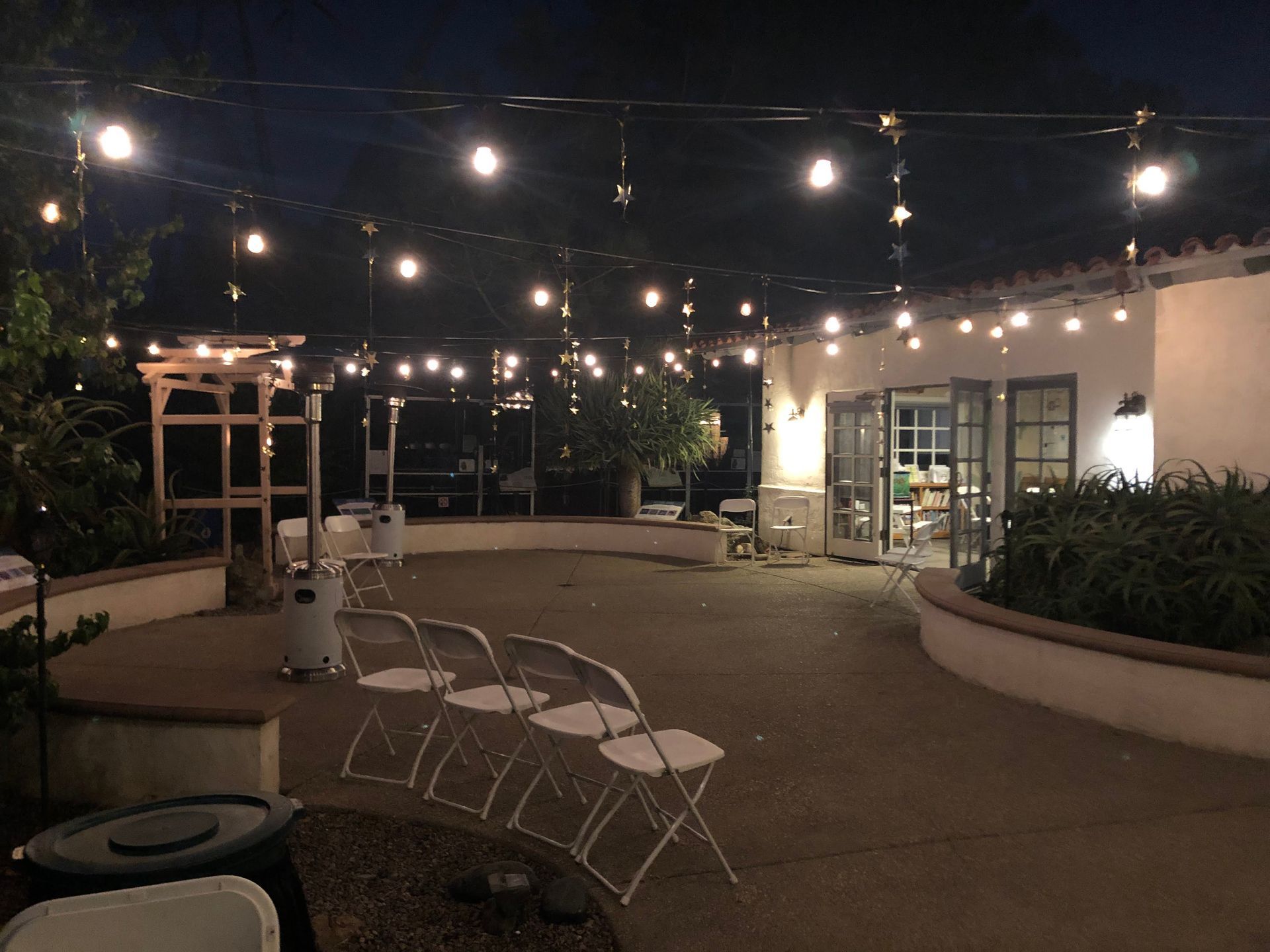 String lights illuminate an outdoor patio at night; chairs are set up near an open doorway.