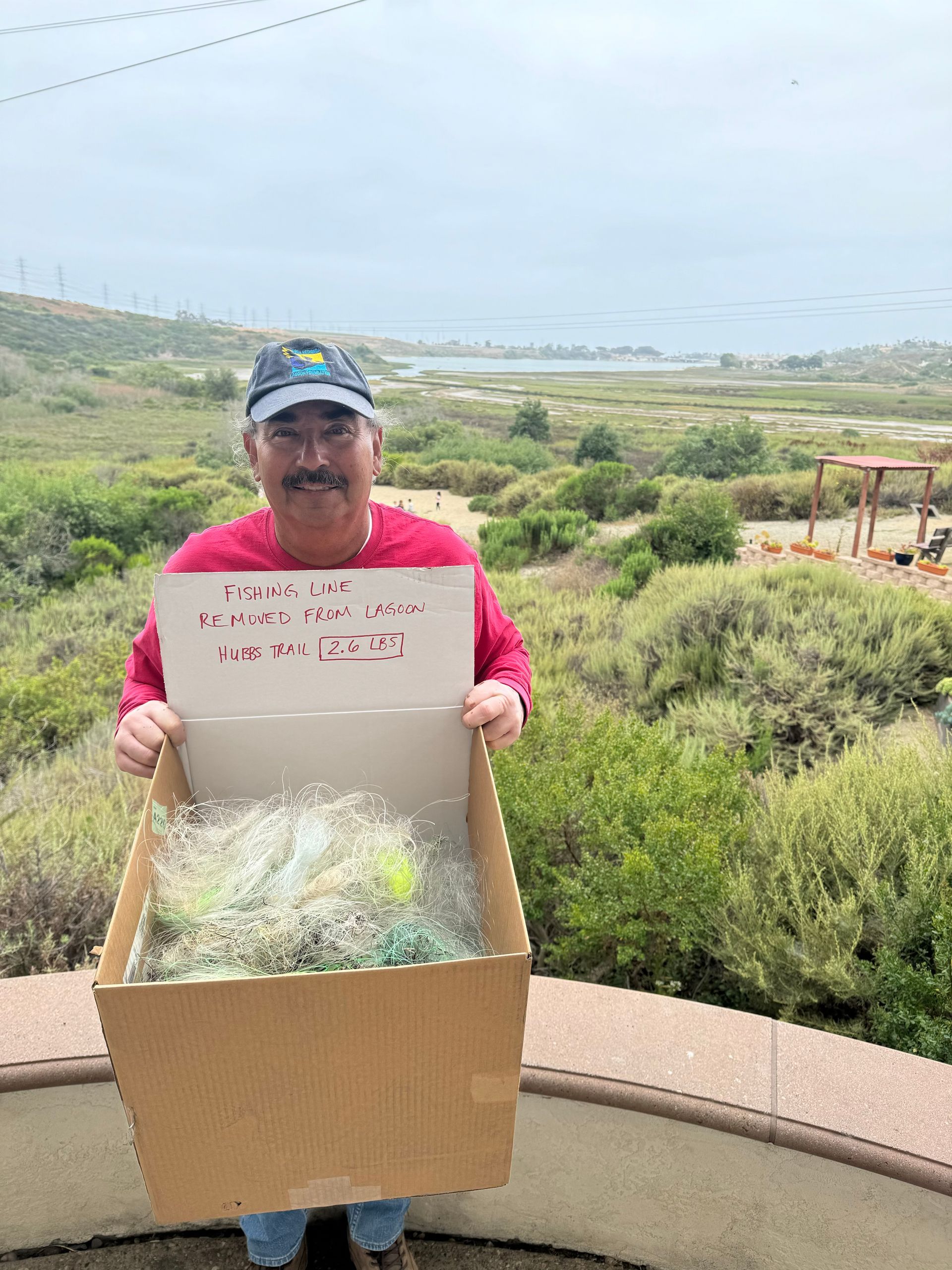 Man holding box of trash, standing outdoors; sign says