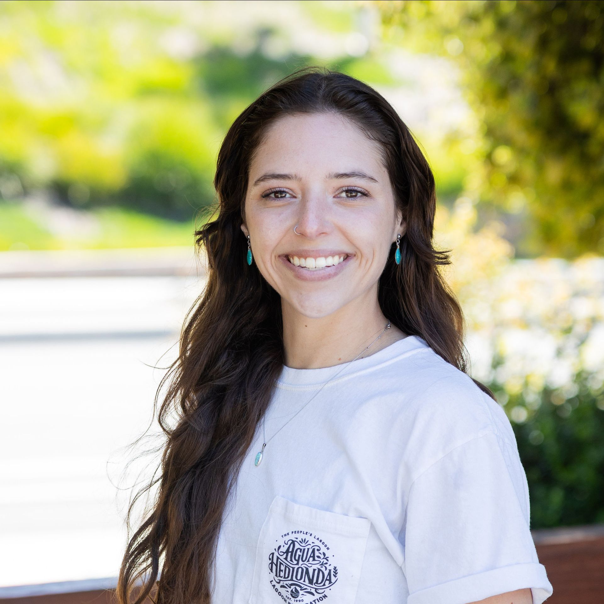 Woman with brown hair and a light blue shirt smiles outdoors.