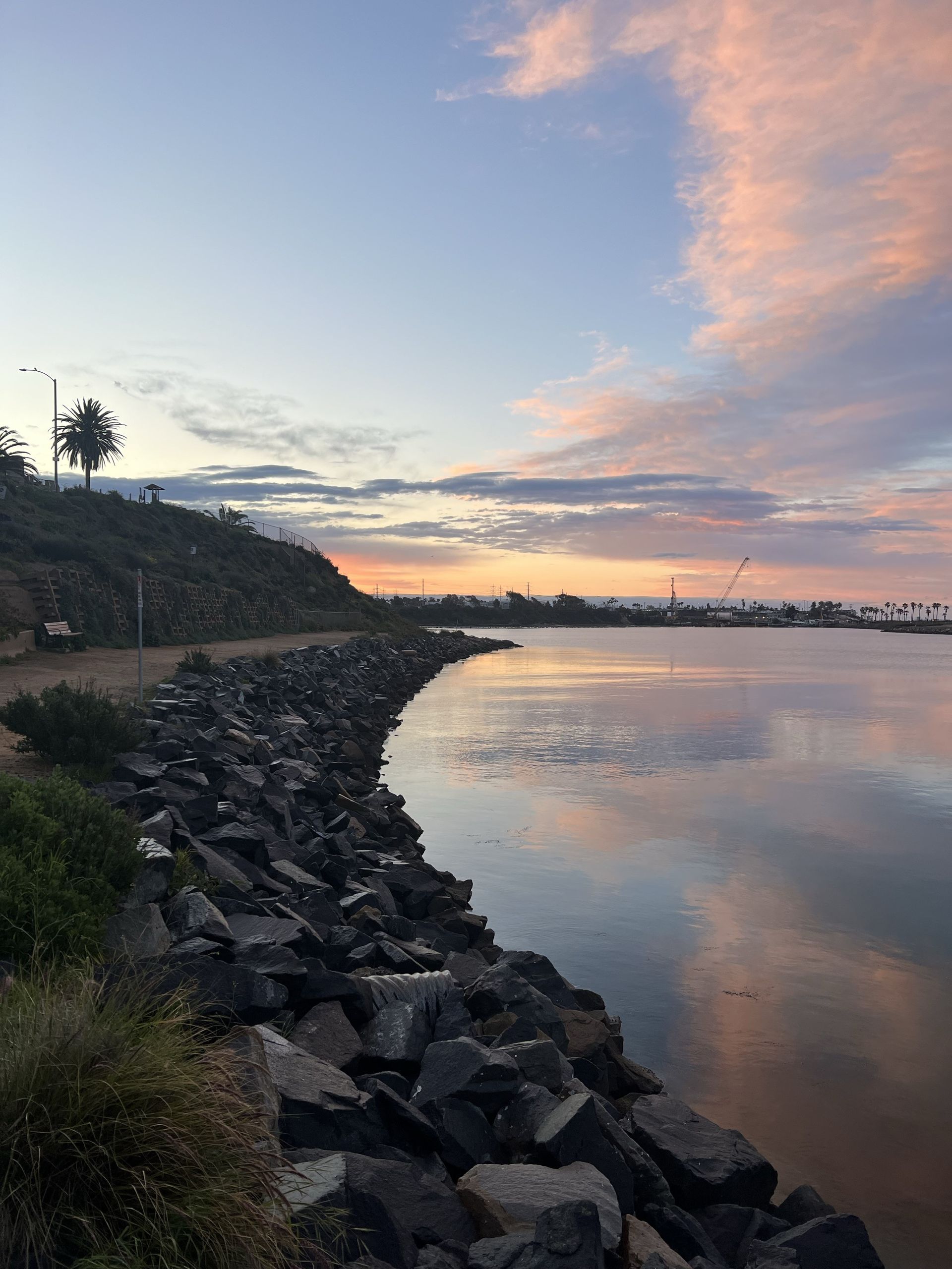 Sunset over calm water reflecting the sky; rocky shoreline.