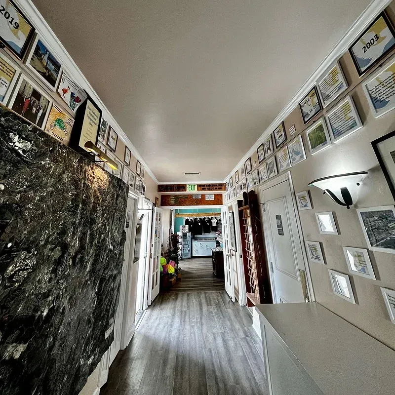 Hallway with awards and a large dark rock on the left wall, leading to a doorway.