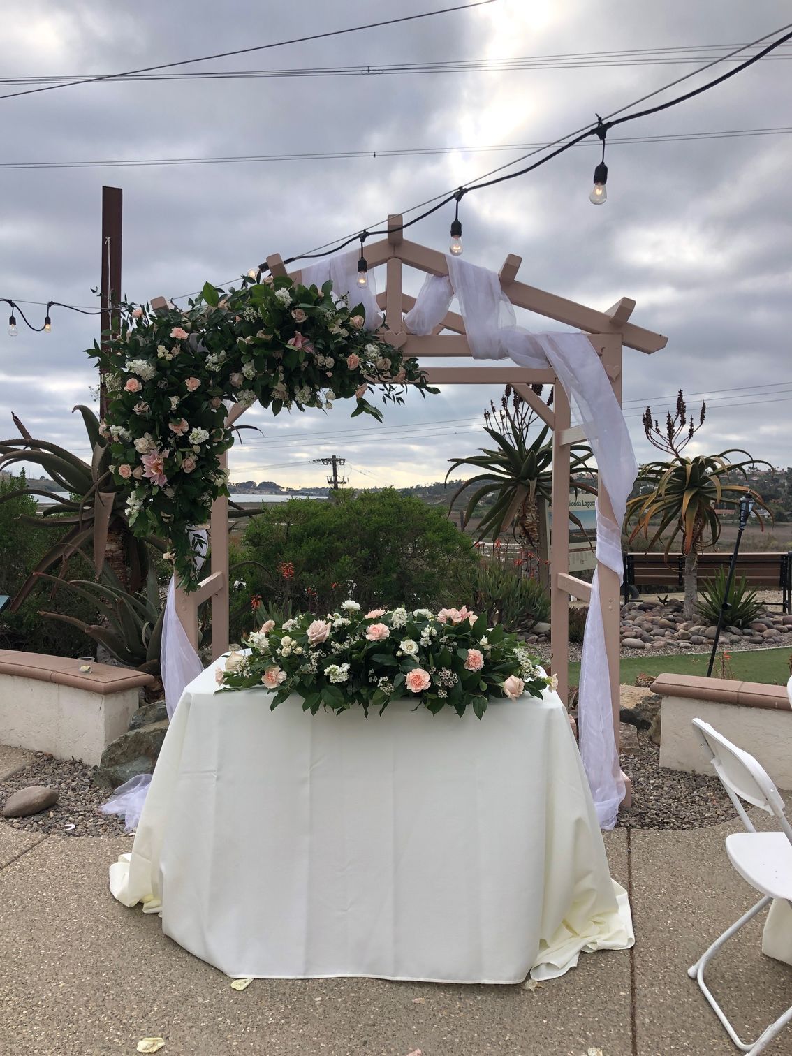 Wedding altar with floral arrangements and draped fabric; cloudy outdoor setting.