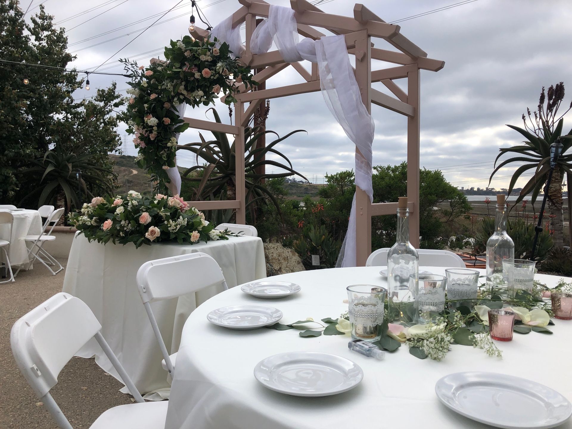 Wedding reception setup with floral arrangements, white linens, and a wooden arch.