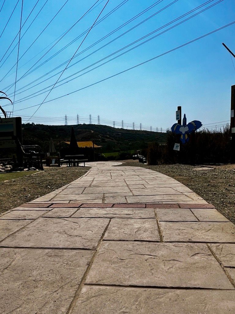 Stone path leading towards a hill, blue sky overhead, power lines.