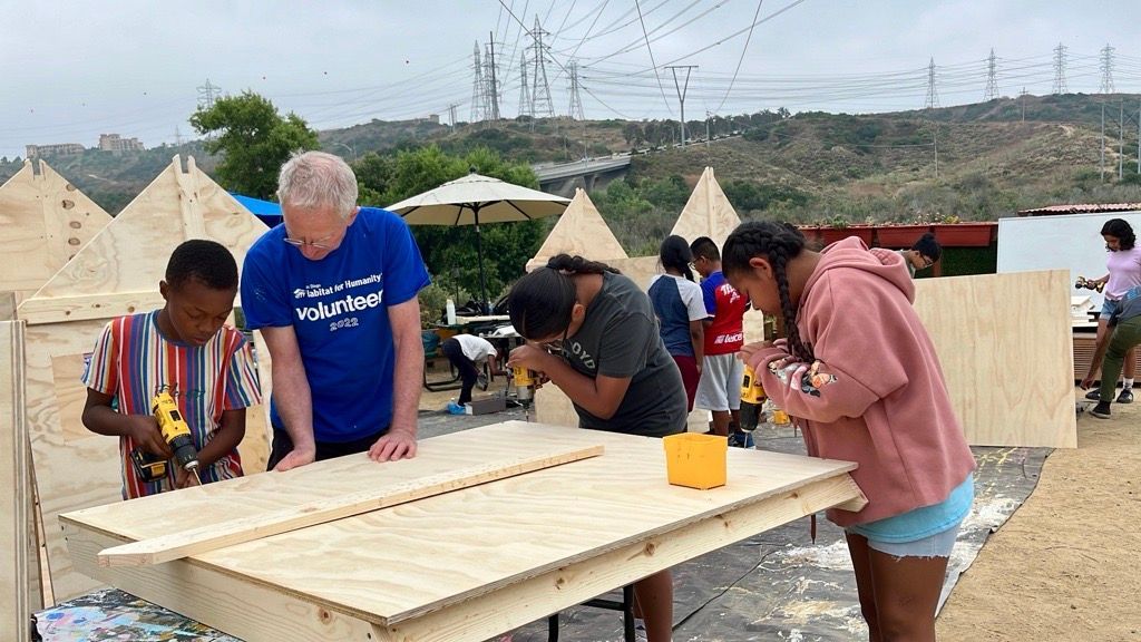 Group of people, including children, building with wood outdoors.