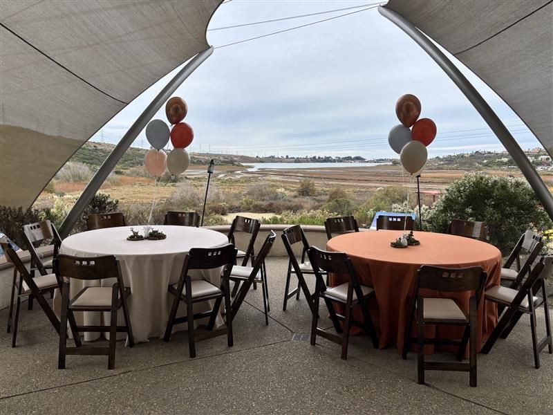 Outdoor event seating, round tables with tablecloths and chairs, balloons, overlooking a landscape.