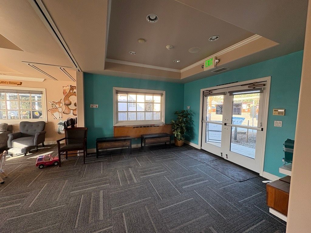 Interior waiting area with teal walls, a window, and double doors leading outside. Gray patterned carpet.