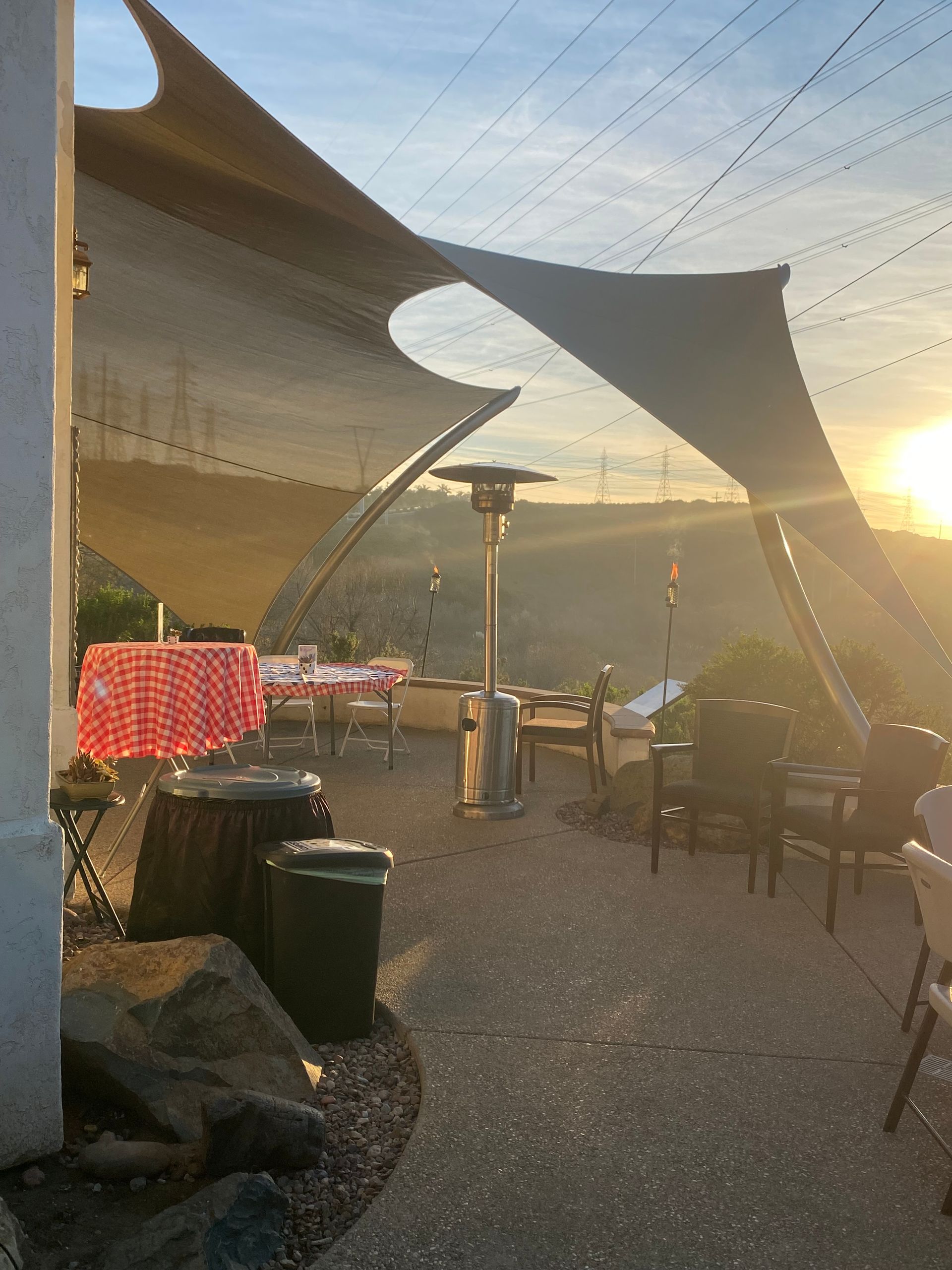 Outdoor restaurant patio with shade sails at sunset overlooking a valley.