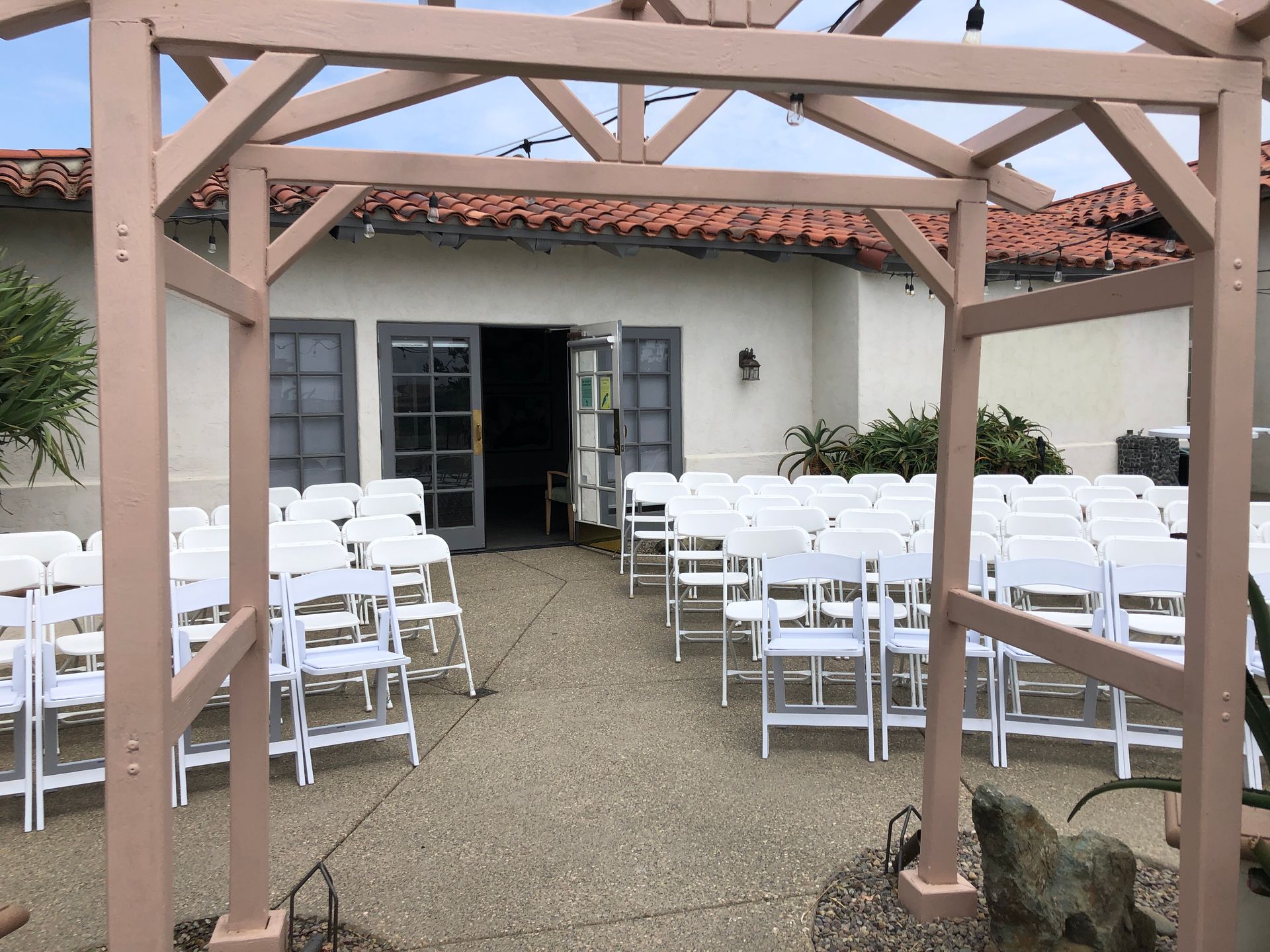 Wedding ceremony setup with white chairs, arch, and open doors.