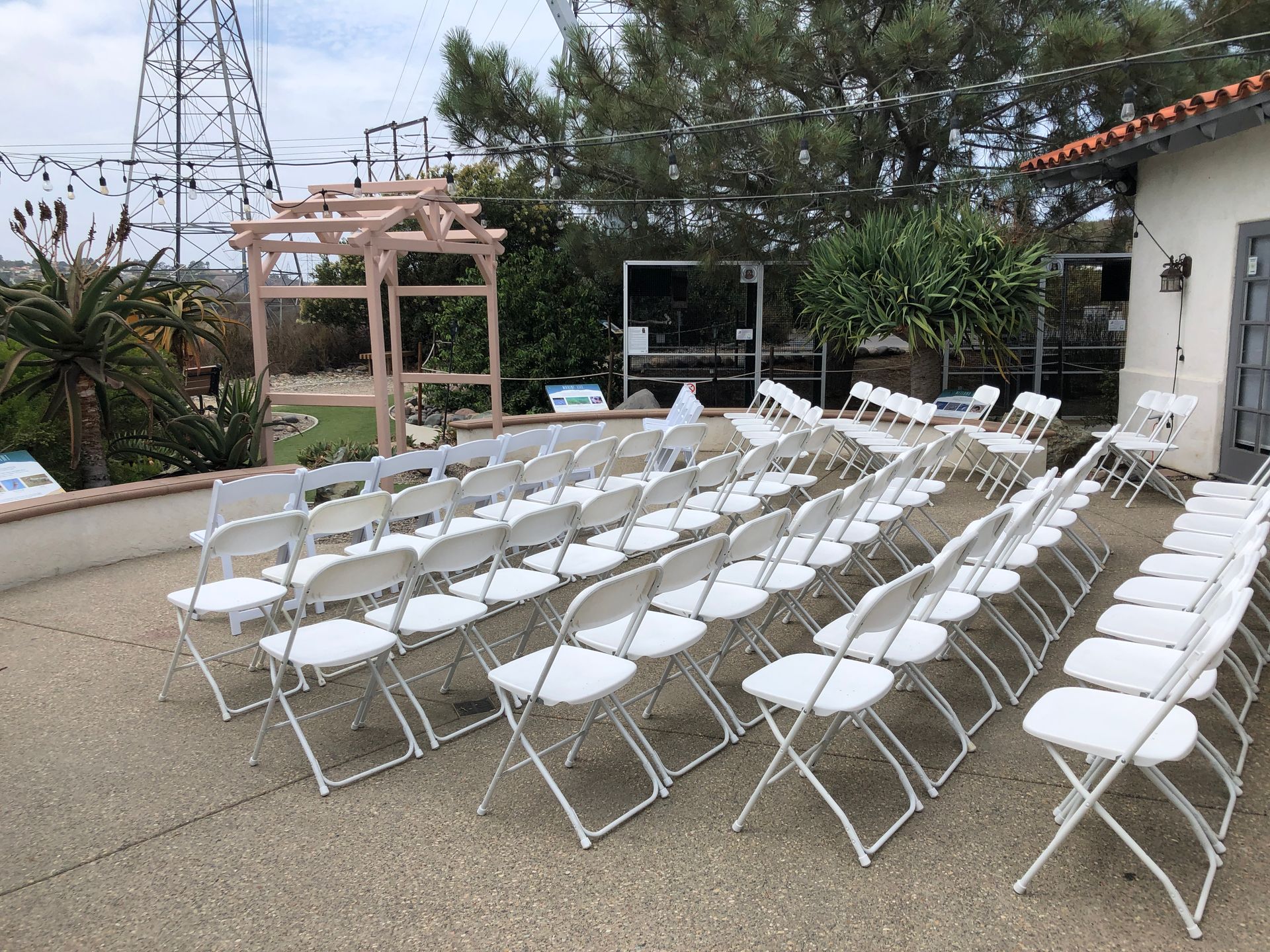 Rows of white folding chairs set up for an outdoor event on a concrete patio.