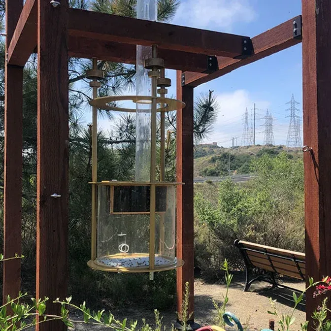 Clear plastic cylinder display suspended in a wooden frame, outdoors.