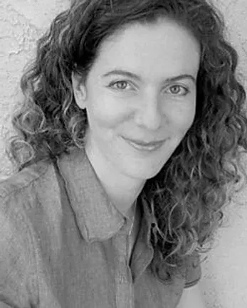Woman with curly hair, smiling, wearing a button-down shirt.