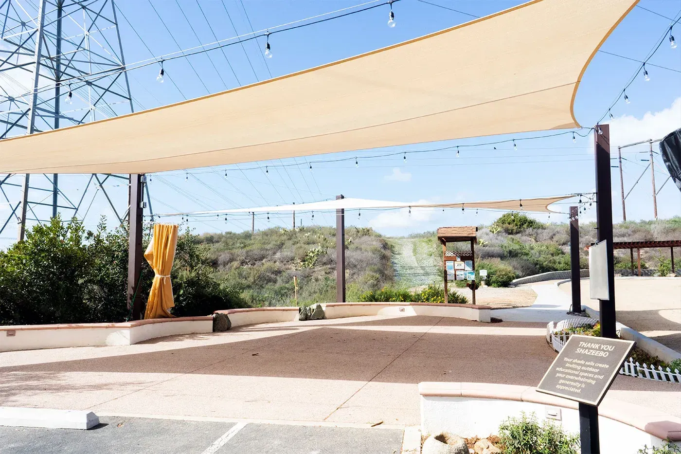 Outdoor patio with beige shade sails, gravel ground, and hillside background.