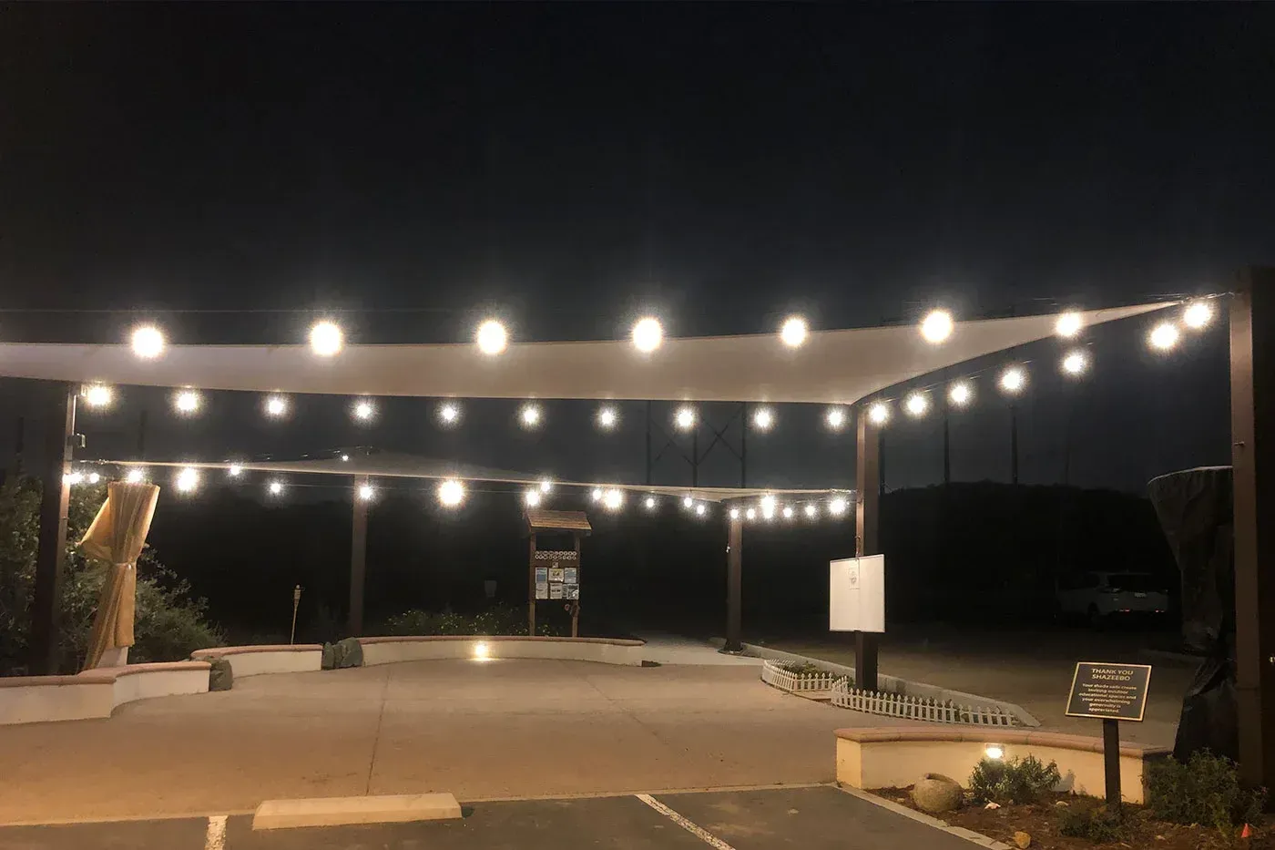 Nighttime scene of an outdoor area with string lights and a canopy over a parking lot.