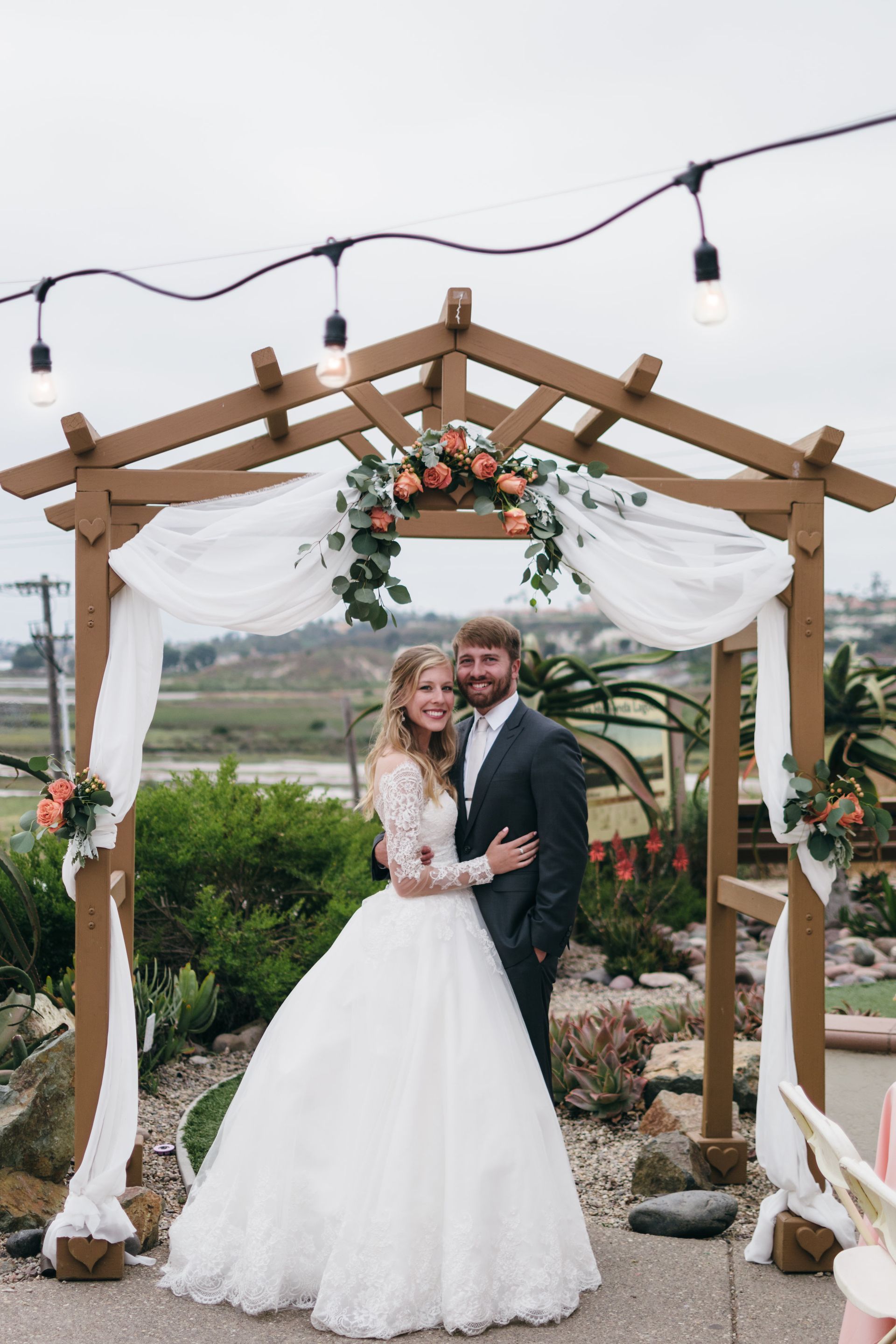 Bride and groom embrace under floral arch, outdoor wedding.