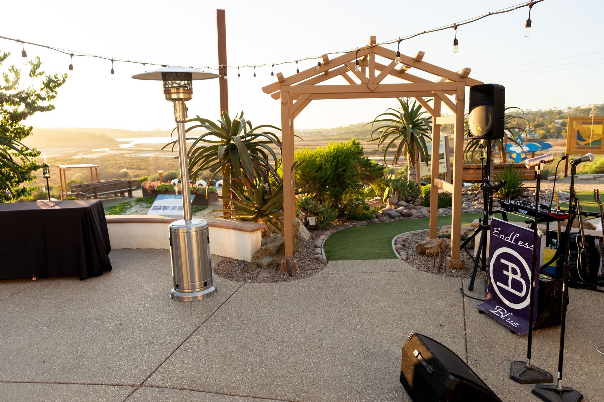 Patio with arbor, heater, sound equipment, and view of landscape at dusk.