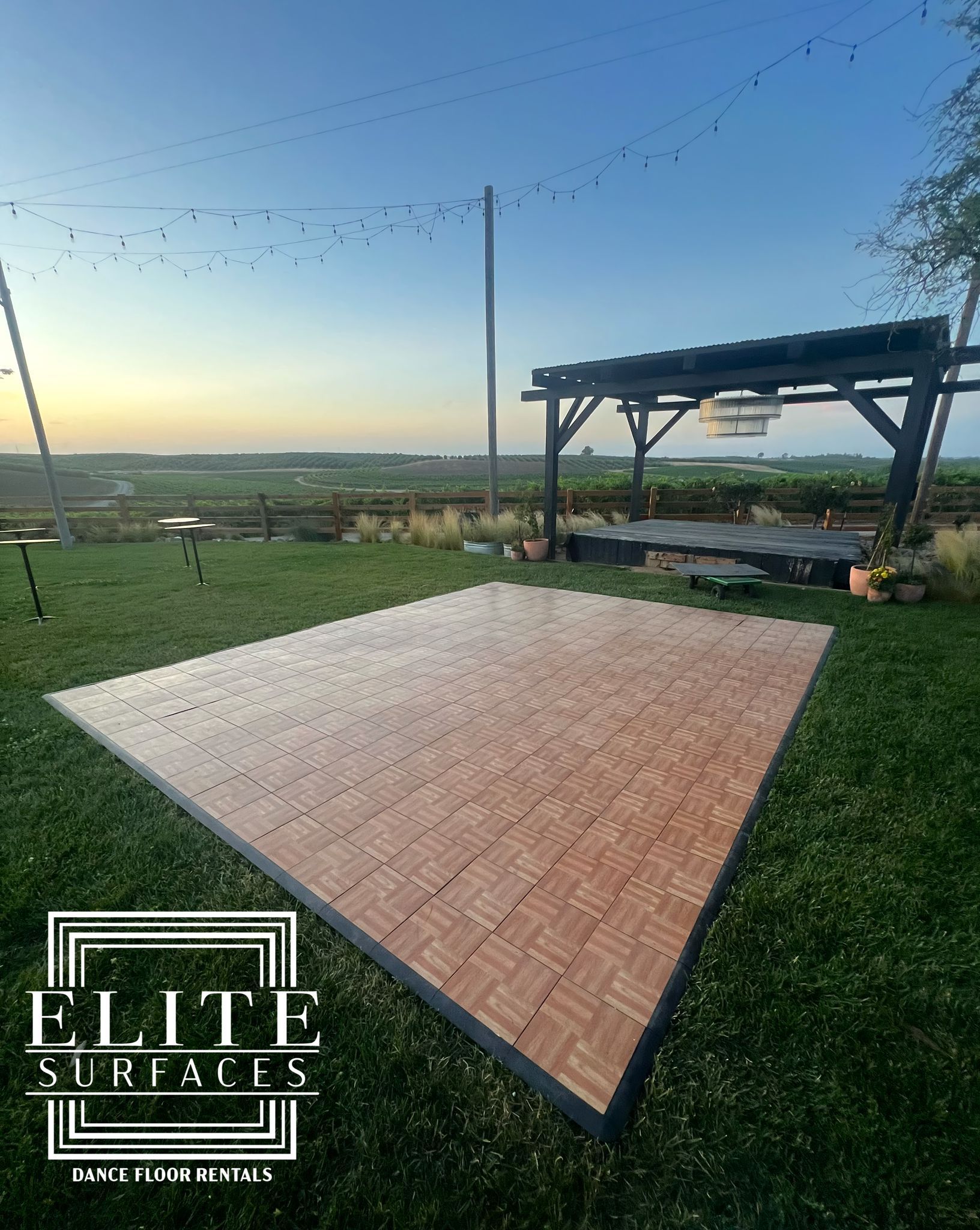 A large wooden dance floor is sitting on top of a lush green field.