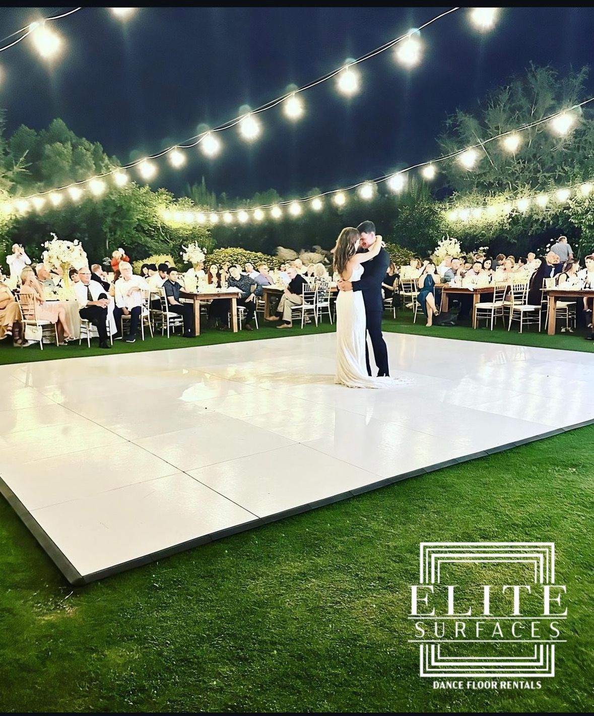 A bride and groom are dancing on a white dance floor.