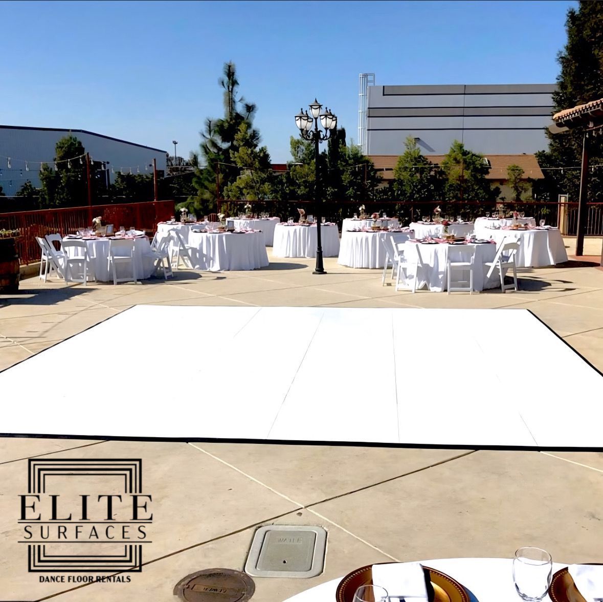 Tables and chairs are set up in front of a white dance floor sponsored by elite surfaces