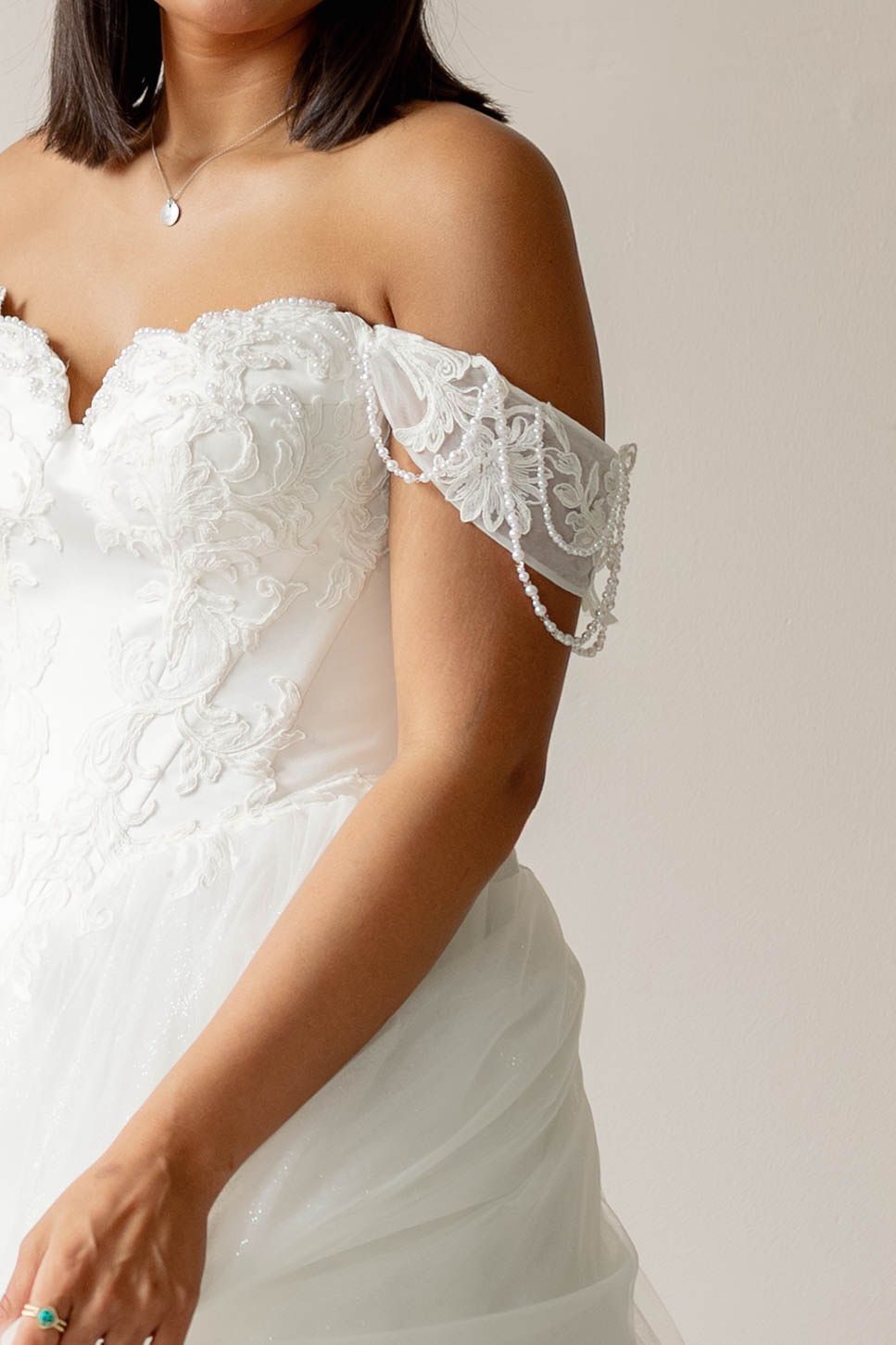 White off-shoulder lace bridal gown with sheer sleeves on a person against a plain background