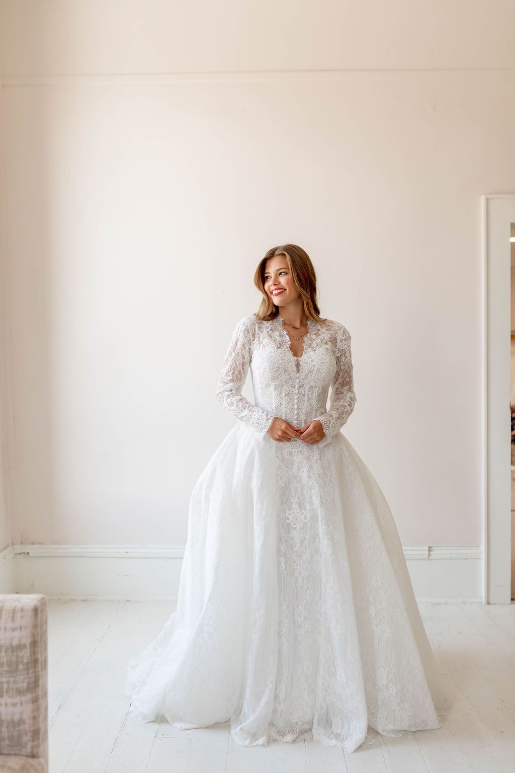 Woman in a white lace wedding gown standing in a bright minimalist room