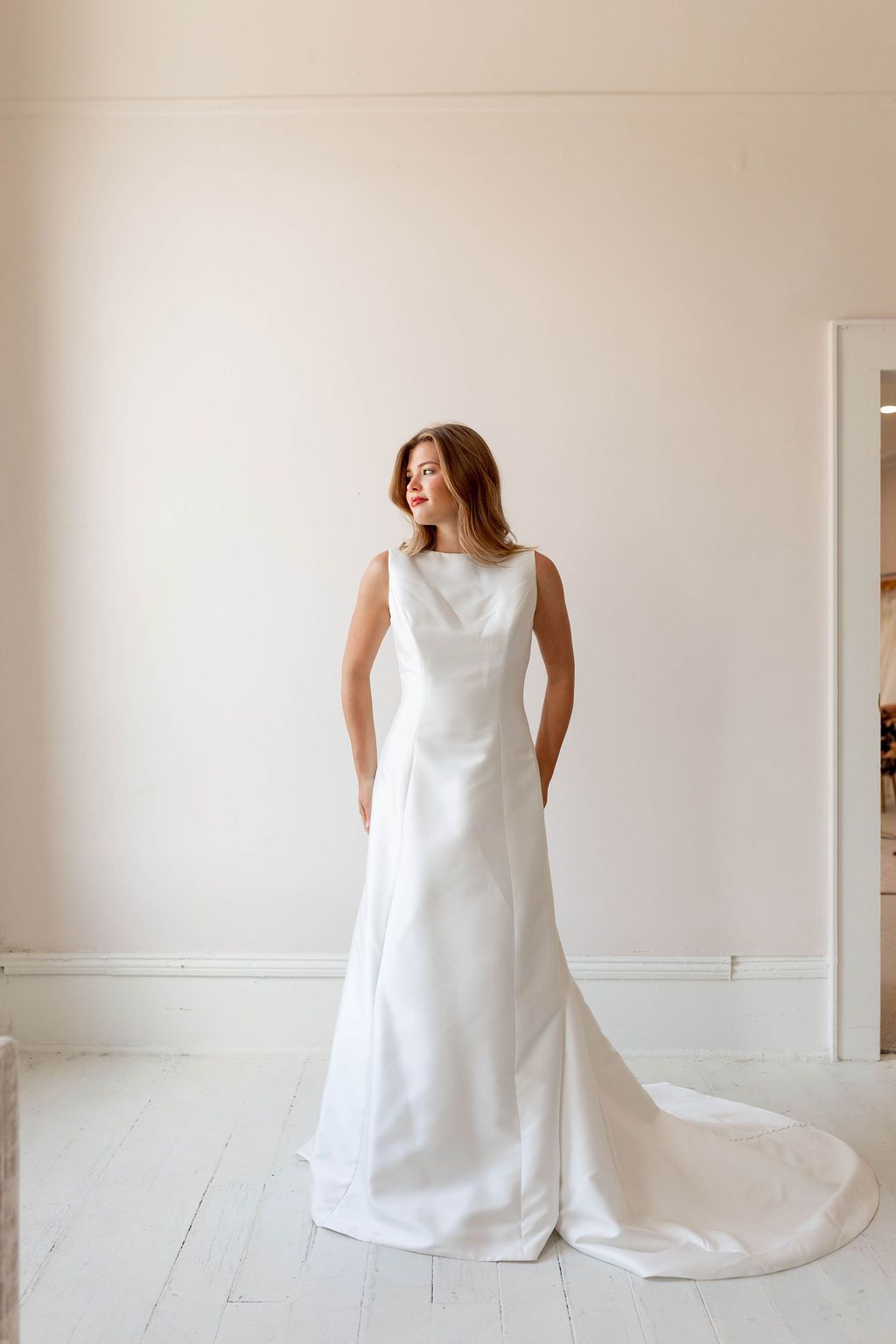 Woman in a white sleeveless dress standing in a bright minimal room with a long train