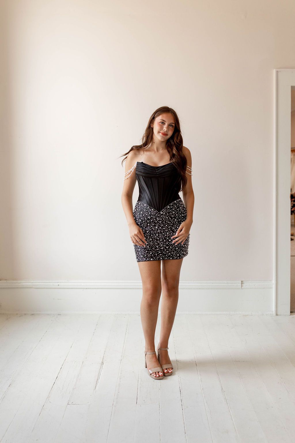 Woman standing in a white room wearing a black top and patterned skirt