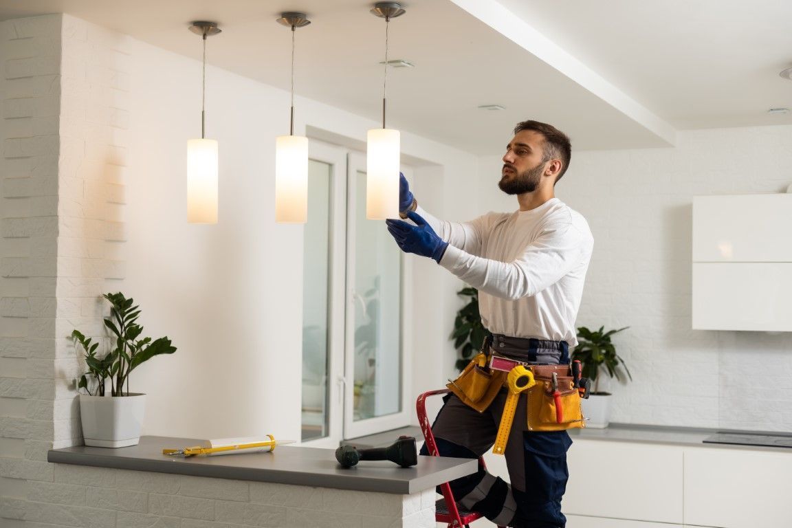 Electrician installing a hanging light fixture in a modern kitchen or dining area.