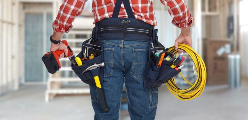 Construction worker holding tools and a yellow coiled cable in a hallway under renovation