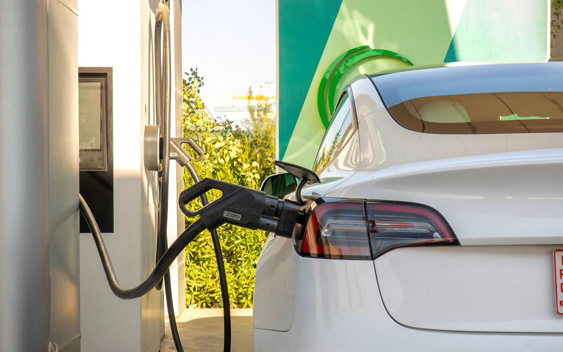 White electric car charging at a station with a black cable plugged into the rear side.
