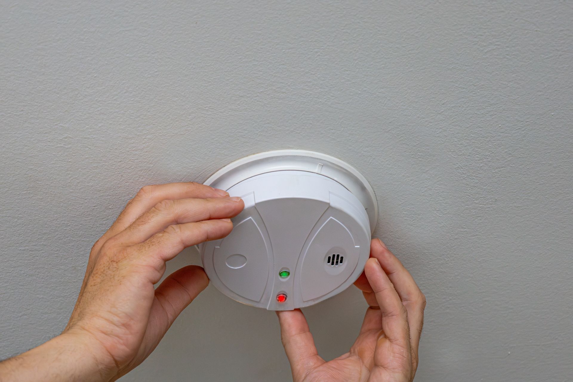 Hands installing a white smoke detector on a ceiling. Hands installing a white smoke detector on a ceiling.