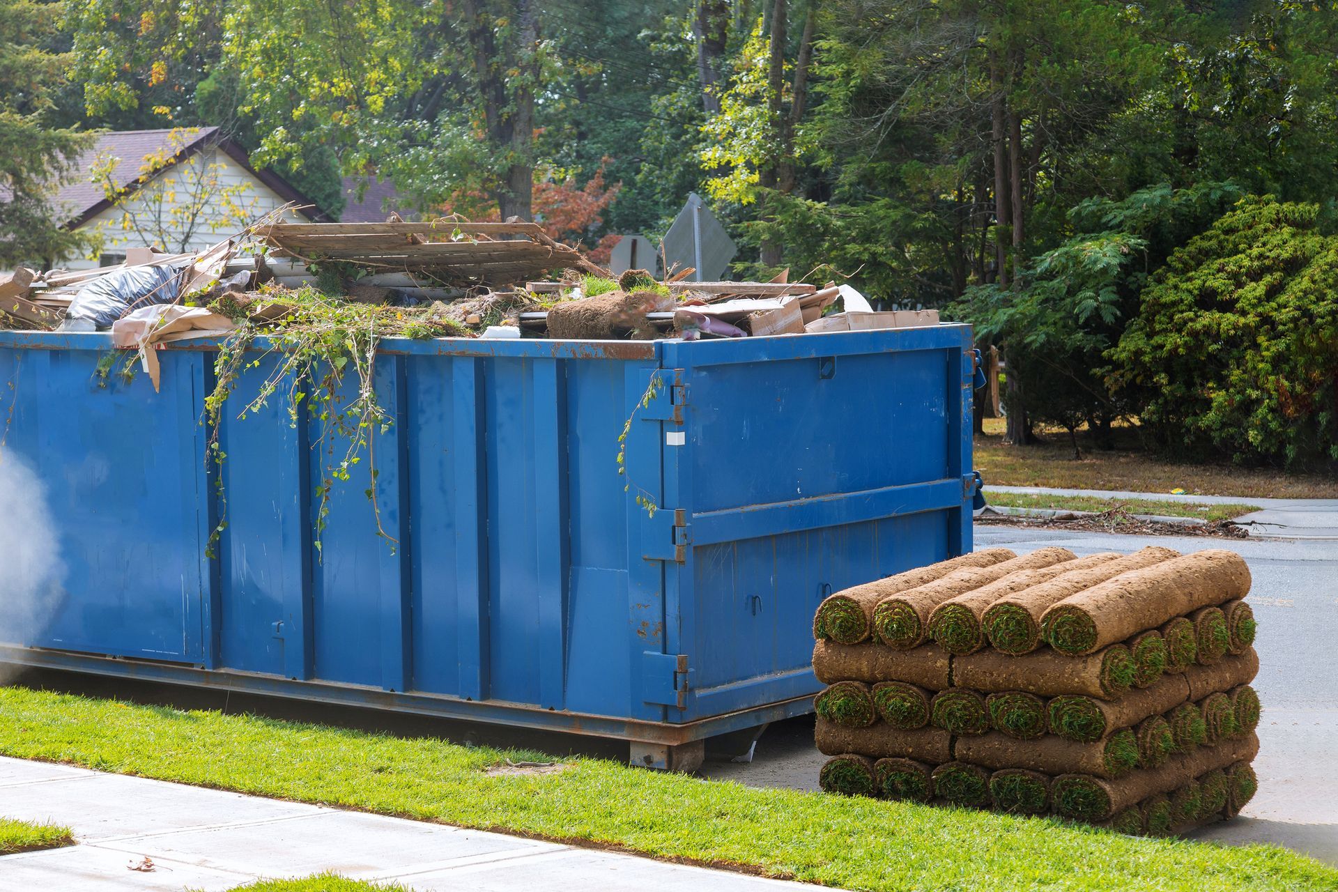 A blue dumpster with a pile of grass next to it.