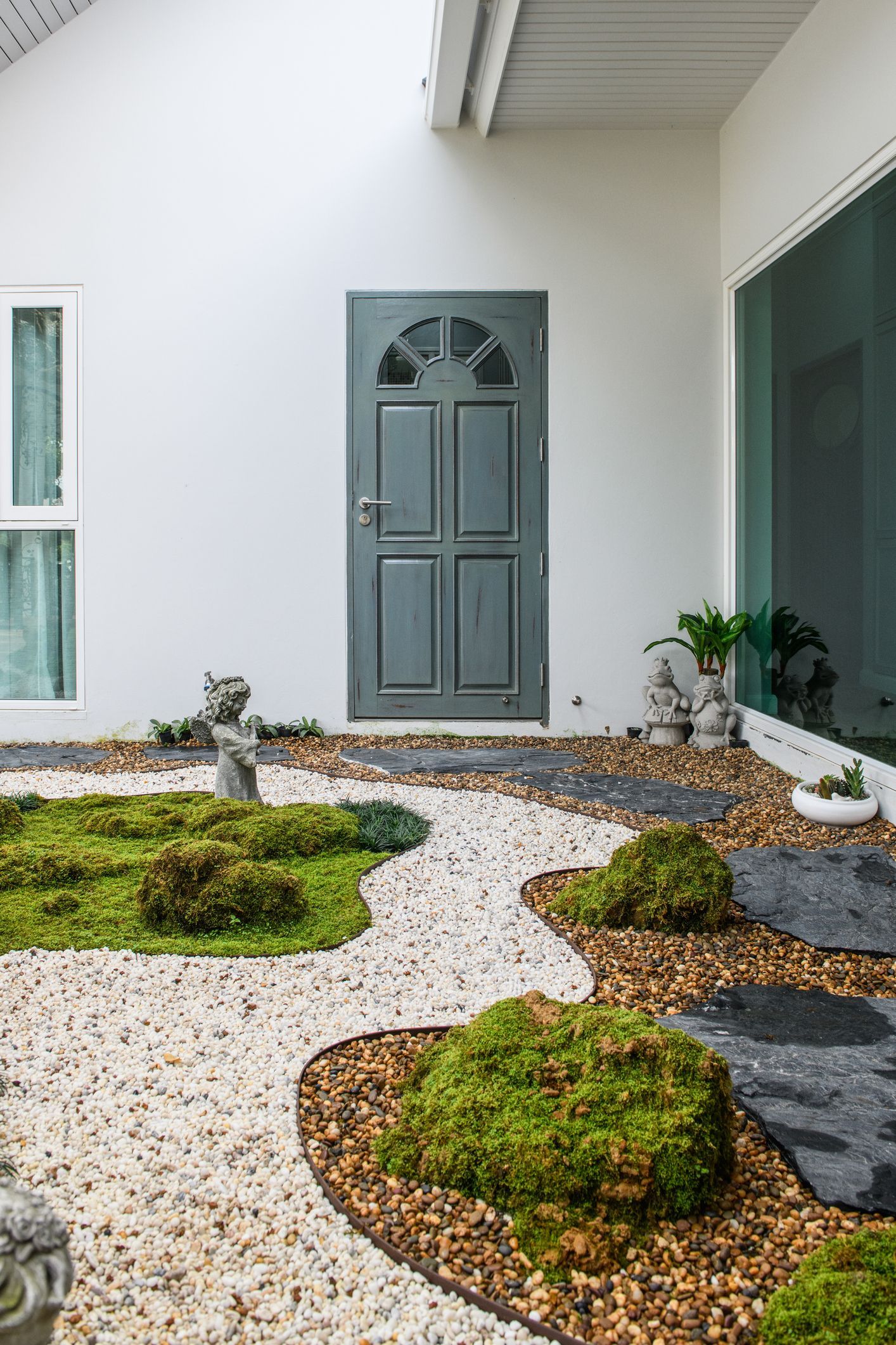 A white house with a gray door and a garden in front of it.